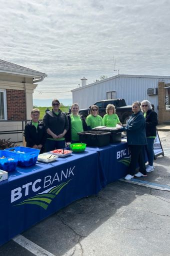 A group of BTC Bank employees standing outside in front of tables smiling
