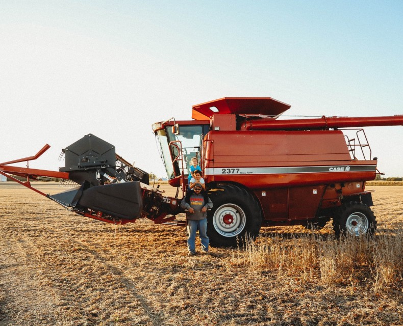 Dad with his kids on his shoulders posing infront of a combine