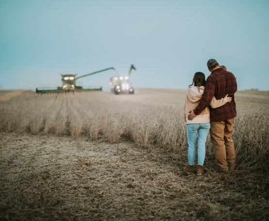 a family stands in a field at dusk watching a combine