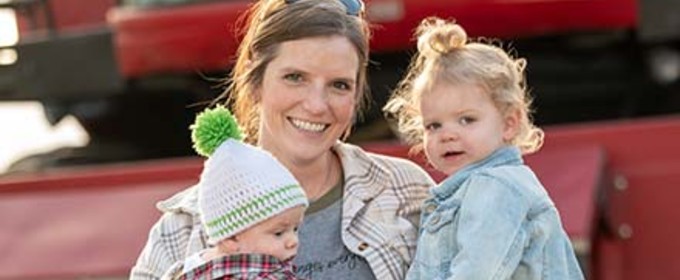 Mother holding her children in front of farm equipment