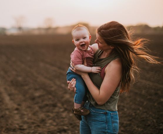 Mom and child in a farm field at dusk.