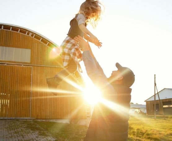 A father tossing a young girl up in the air lovingly at sunset in front of a barn