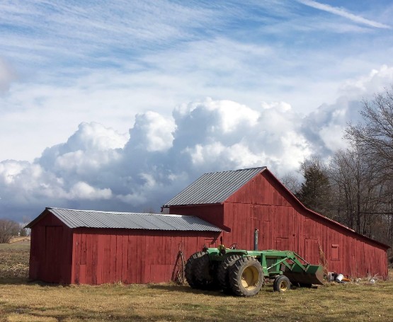 a tractor sits in front of an old bar with billowing clouds in the distance