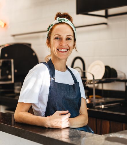 A smiling barista leaning on the counter of a coffee shop