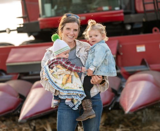 Mom and two kids with farm equipment in the background.
