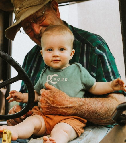 a grandfather holds his newborn grandchild while sitting in a tractor