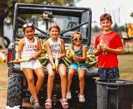 Four kids shucking corn sitting in a ATV.