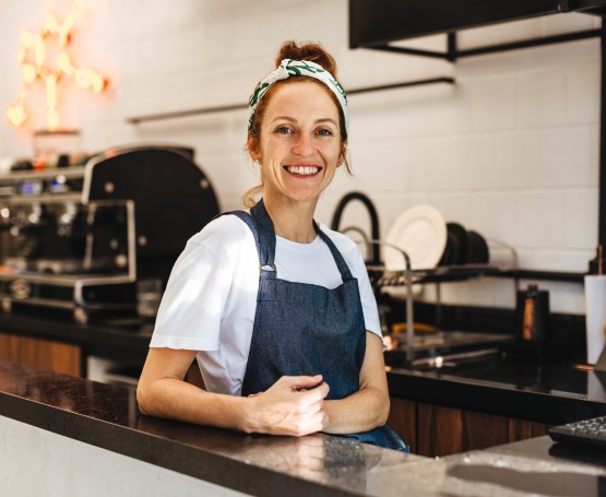 A barista stands smiling behind the counter of a coffee shop
