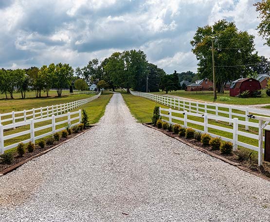 Gravel path with fences and grassy fields.