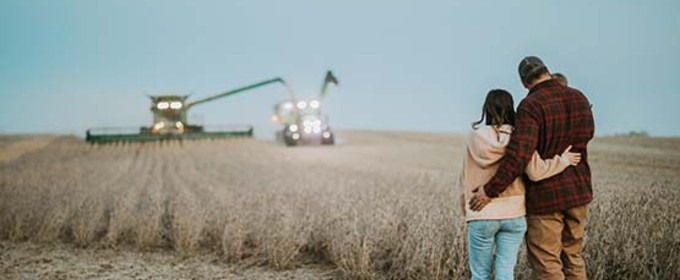 Couple holding each other standing in a wheat field that's being harvested