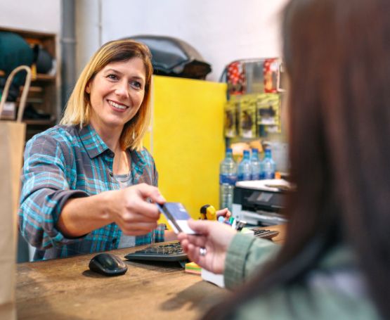 A smiling blonde cashier returning a credit card to the customer after making a purchase.